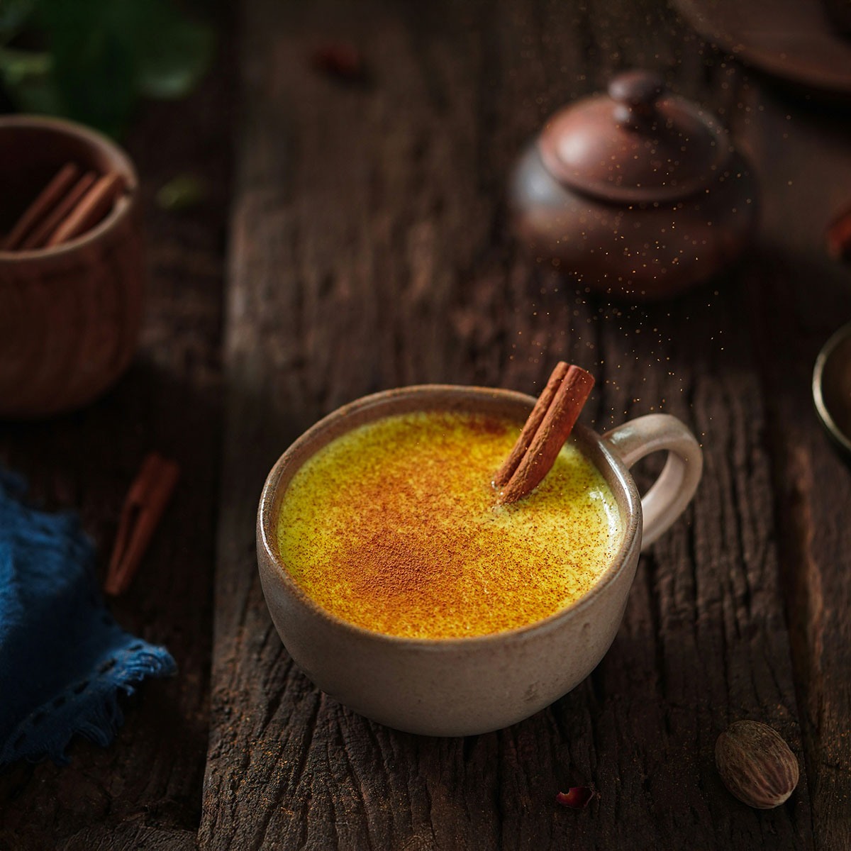 Ceramic cup filled with golden milk, garnished with cinnamon powder and a cinnamon stick, placed on a rustic wooden table.