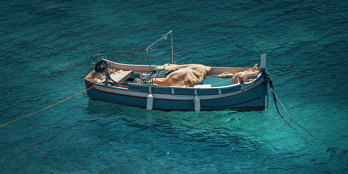 A small fishing boat with beige nets floats calmly on crystal-clear turquoise water, secured by ropes.