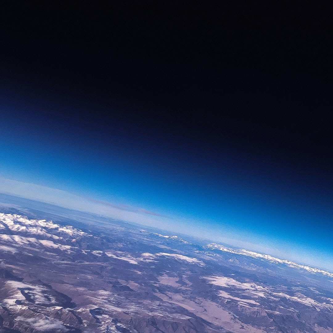 View from the stratosphere showing the curvature of Mother Earth with mountains and atmosphere fading into space.