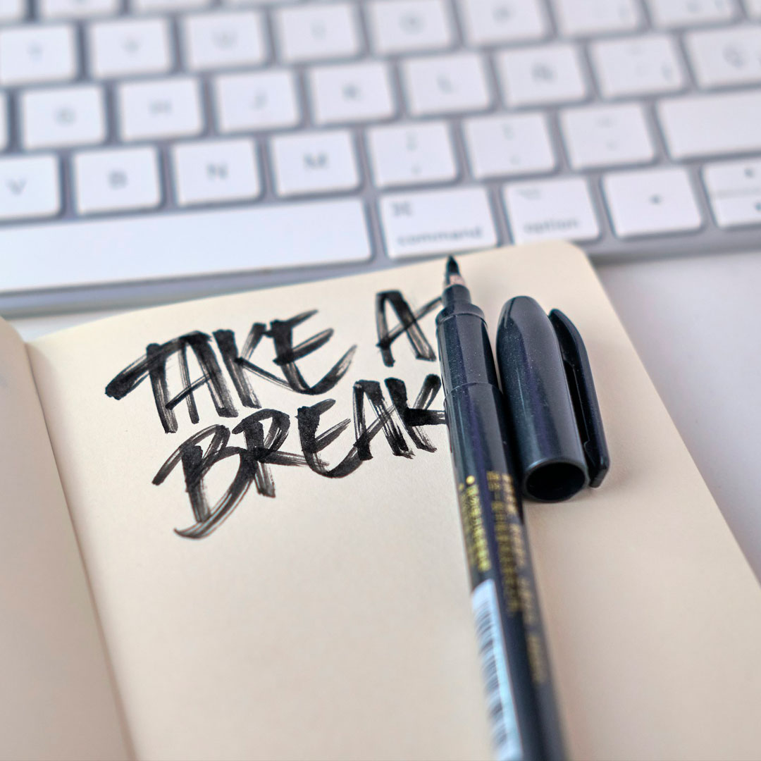 Notebook with “TAKE A BREAK” written in bold lettering next to a marker, with a computer keyboard in the background.