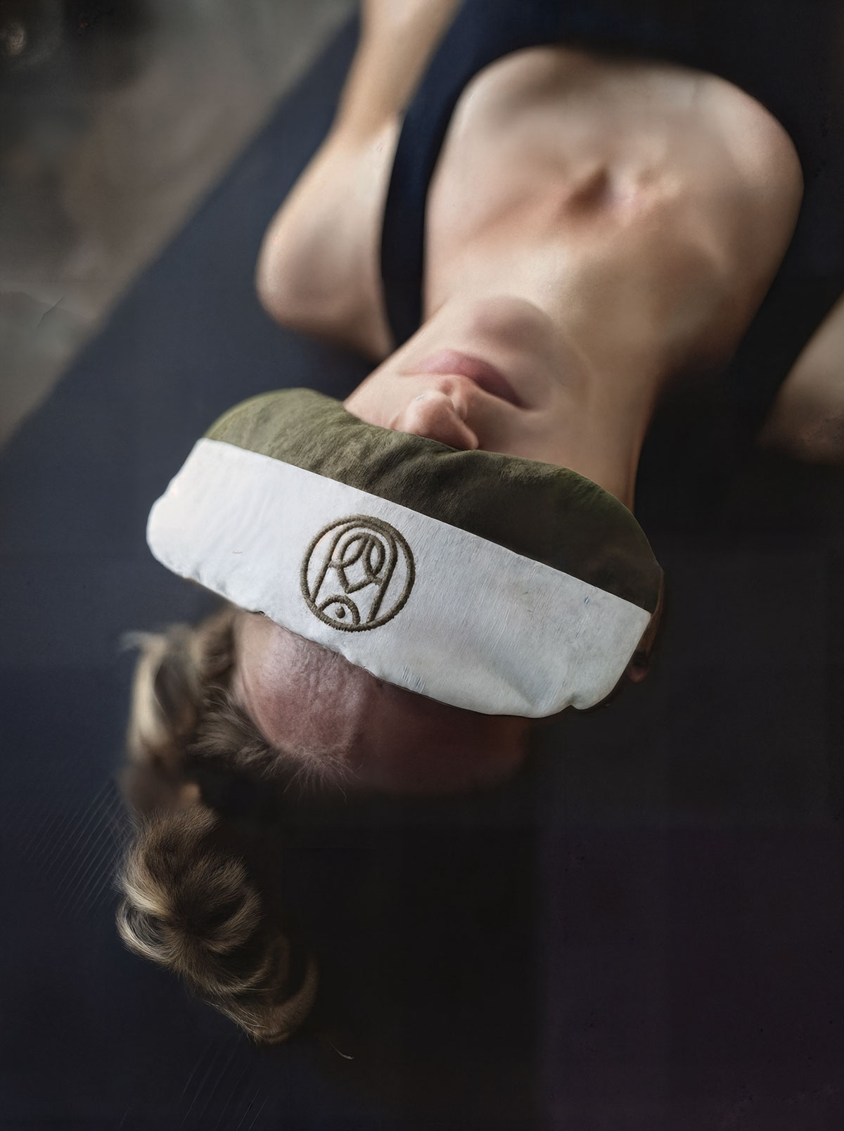 Person resting on a yoga mat with a branded eye pillow during Yoga Nidra, capturing a calm, deep-relaxation moment.